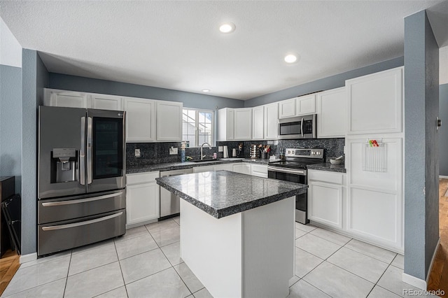 kitchen featuring a sink, white cabinets, appliances with stainless steel finishes, a center island, and dark countertops