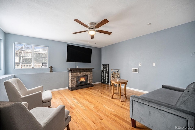 living room with a fireplace, visible vents, a ceiling fan, wood finished floors, and baseboards