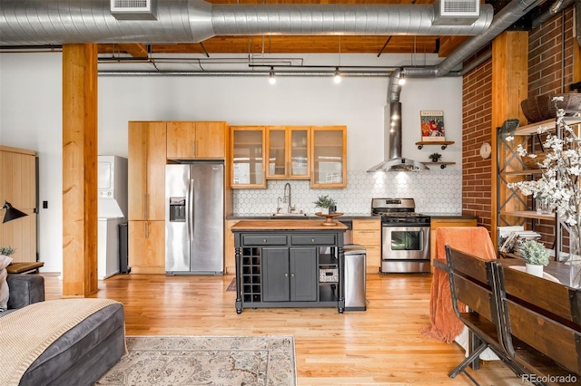2955 Inca St Unit 2P, Denver, CO 80202 - kitchen featuring appliances with stainless steel finishes, stacked washing machine and dryer, light wood-style flooring, island exhaust hood, and backsplash