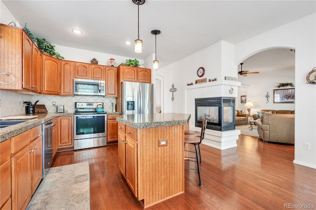 kitchen featuring appliances with stainless steel finishes, hardwood / wood-style floors, a multi sided fireplace, and tasteful backsplash