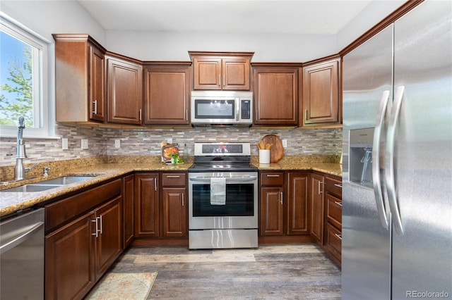 kitchen featuring stainless steel appliances, a sink, light wood-type flooring, light stone countertops, and decorative backsplash