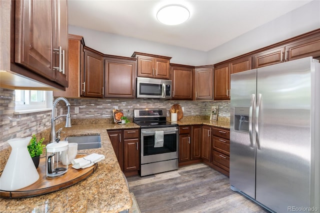 kitchen with stainless steel appliances, a sink, light wood-style flooring, and light stone counters