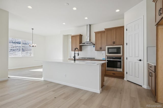 kitchen with a center island with sink, wall chimney exhaust hood, decorative backsplash, appliances with stainless steel finishes, and decorative light fixtures