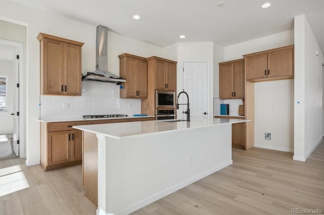 kitchen featuring wall chimney exhaust hood, sink, a kitchen island with sink, and appliances with stainless steel finishes