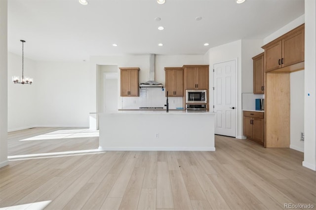 kitchen featuring wall chimney exhaust hood, stainless steel appliances, backsplash, a chandelier, and a kitchen island with sink