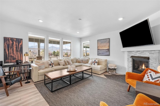 living room with recessed lighting, a stone fireplace, and light wood-style floors