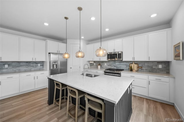 kitchen featuring a sink, stainless steel appliances, a kitchen breakfast bar, light wood-style floors, and decorative backsplash