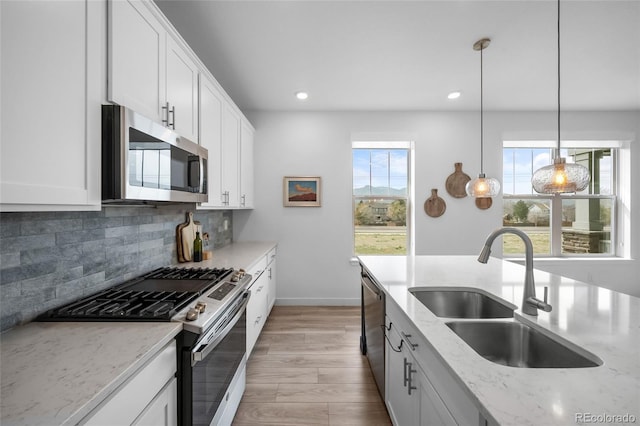 kitchen with decorative backsplash, light stone countertops, a sink, light wood finished floors, and stainless steel appliances