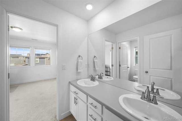 bathroom featuring toilet, baseboards, double vanity, and a sink
