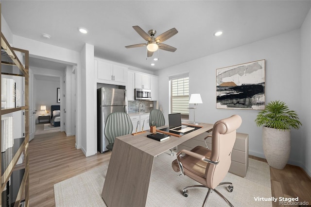 home office with a sink, baseboards, a ceiling fan, and light wood-style flooring