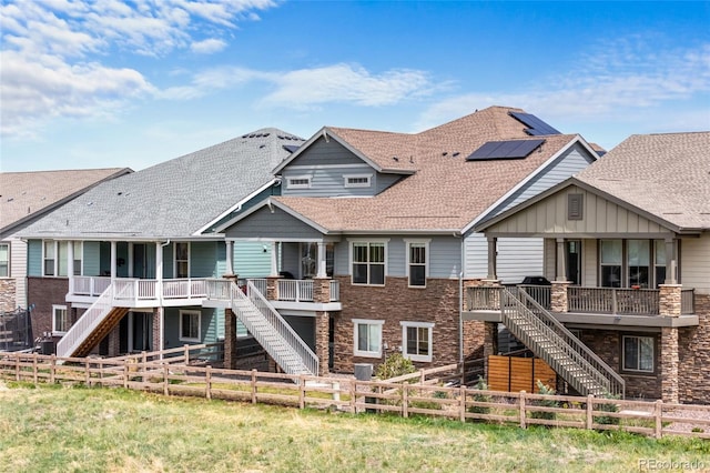 back of property with stairway, roof with shingles, a fenced backyard, and stone siding