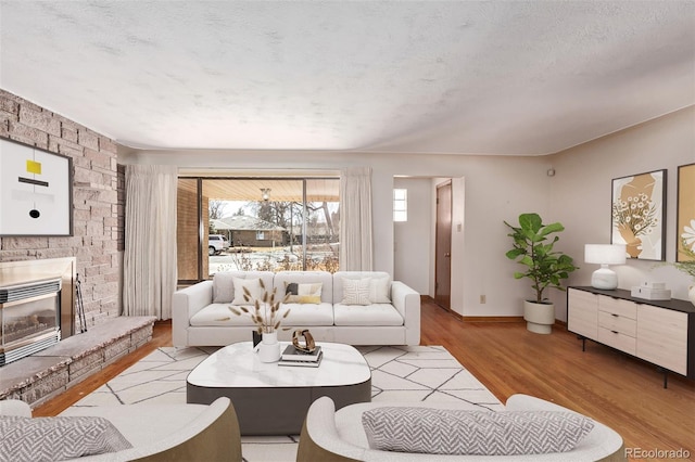 living room featuring a textured ceiling, a stone fireplace, wood finished floors, and baseboards