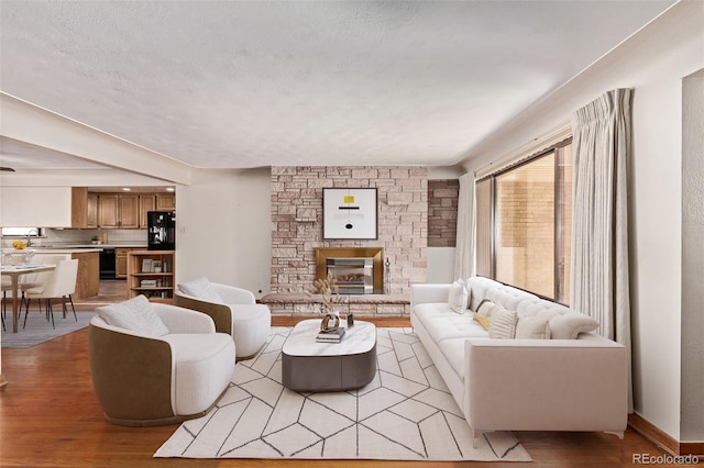 living room featuring light wood-type flooring, baseboards, a textured ceiling, and a stone fireplace