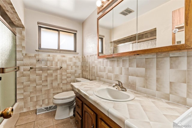 bathroom featuring toilet, a shower with door, visible vents, and tile walls