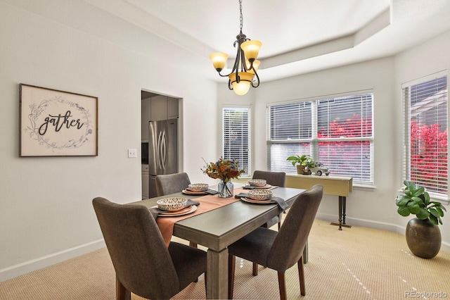 carpeted dining area with a notable chandelier and a raised ceiling