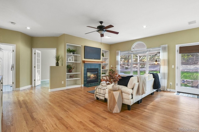 living room with ceiling fan, a tile fireplace, plenty of natural light, and light wood-type flooring