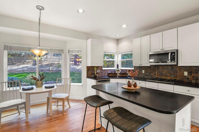 kitchen with a healthy amount of sunlight, light hardwood / wood-style floors, stainless steel appliances, and hanging light fixtures