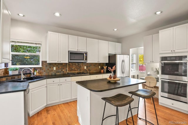 kitchen with stainless steel appliances, sink, light wood-type flooring, and white cabinets