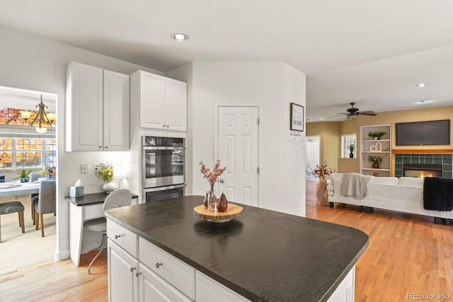 kitchen with ceiling fan with notable chandelier, white cabinetry, a tile fireplace, and light wood-type flooring