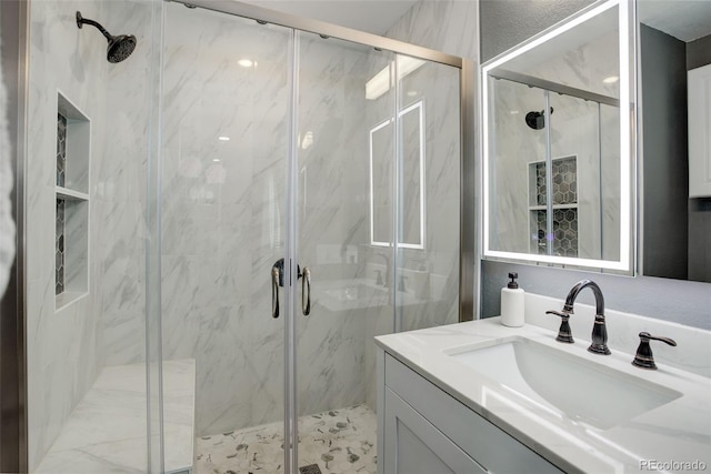 bathroom with a textured wall, a marble finish shower, and vanity