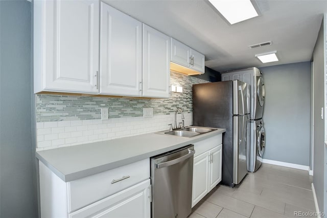 kitchen featuring stainless steel appliances, stacked washer / dryer, light countertops, and white cabinetry