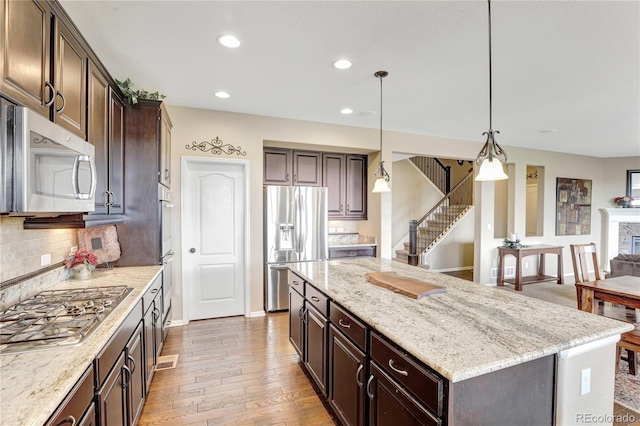 kitchen featuring dark brown cabinetry, appliances with stainless steel finishes, light stone counters, tasteful backsplash, and a kitchen island