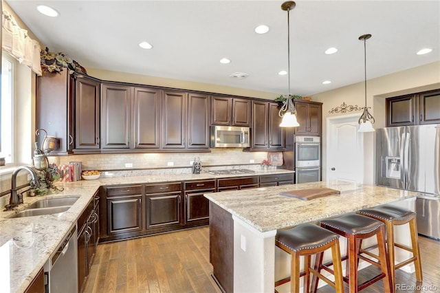 kitchen with dark brown cabinets, a center island, hardwood / wood-style flooring, a sink, and stainless steel appliances