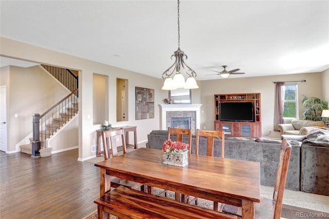 dining space with a ceiling fan, a fireplace, dark wood finished floors, stairway, and baseboards