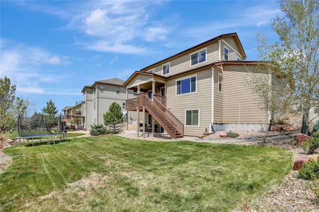 rear view of house featuring a deck, stairs, a patio area, a trampoline, and a yard