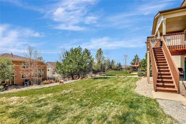 view of yard with a wooden deck, a trampoline, and stairway