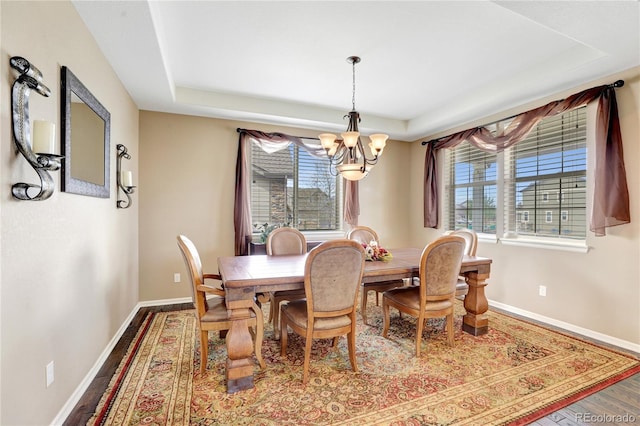 dining space featuring an inviting chandelier, baseboards, wood finished floors, and a tray ceiling