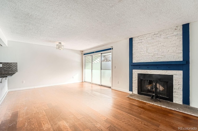 unfurnished living room featuring hardwood / wood-style floors, a stone fireplace, and a textured ceiling