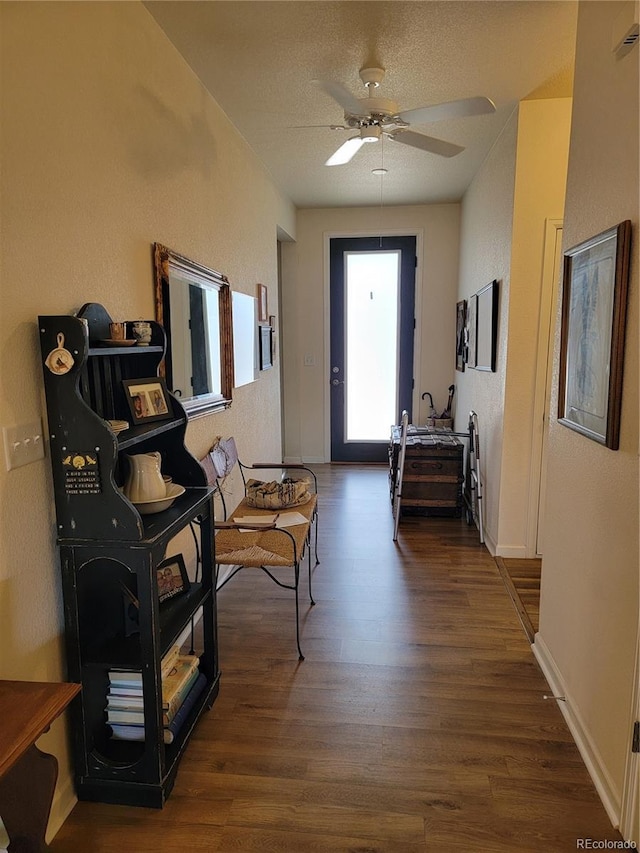 interior space with ceiling fan, a textured wall, a textured ceiling, dark wood-type flooring, and baseboards