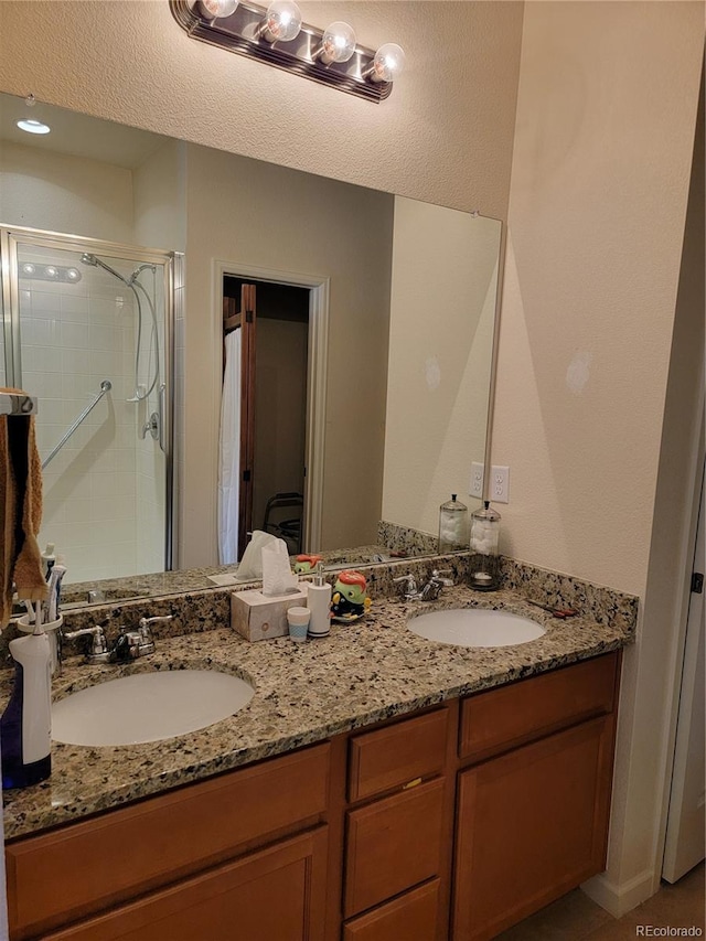 full bathroom with double vanity, a shower stall, and a sink