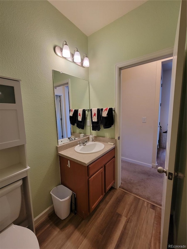 half bathroom featuring toilet, wood finished floors, vanity, and baseboards