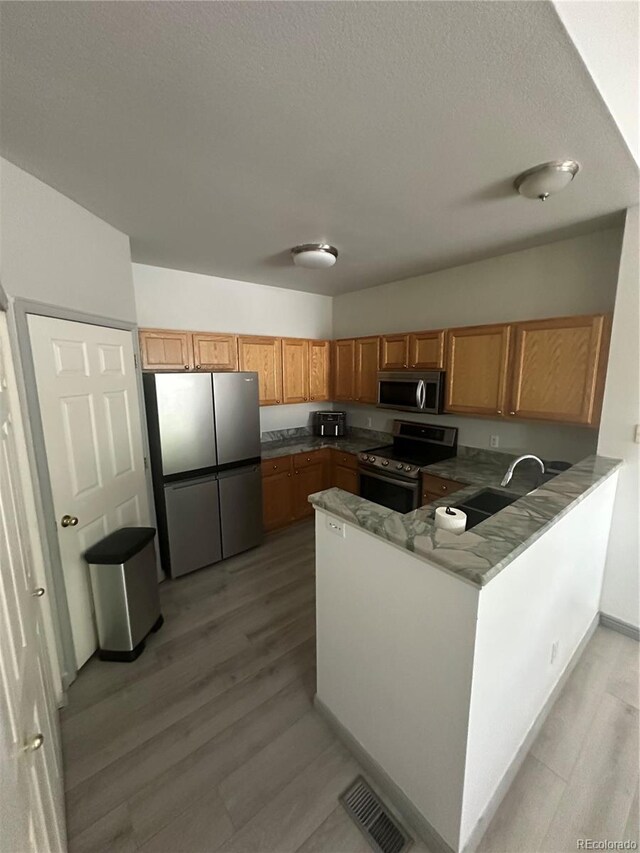 12235 E 2nd Dr, Aurora, CO 80011 - kitchen with stainless steel appliances, light wood-style floors, a peninsula, a textured ceiling, and brown cabinets