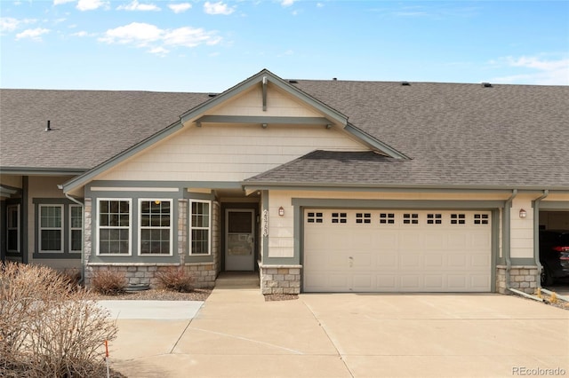 view of front facade with stone siding, an attached garage, roof with shingles, and driveway