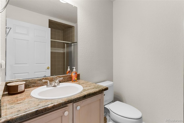 full bath with vanity, toilet, a shower stall, and a textured wall