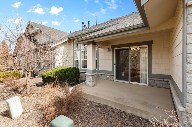 doorway to property with stone siding, a shingled roof, and a patio