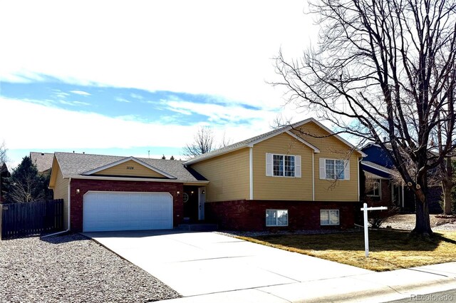 tri-level home featuring brick siding, driveway, fence, and an attached garage