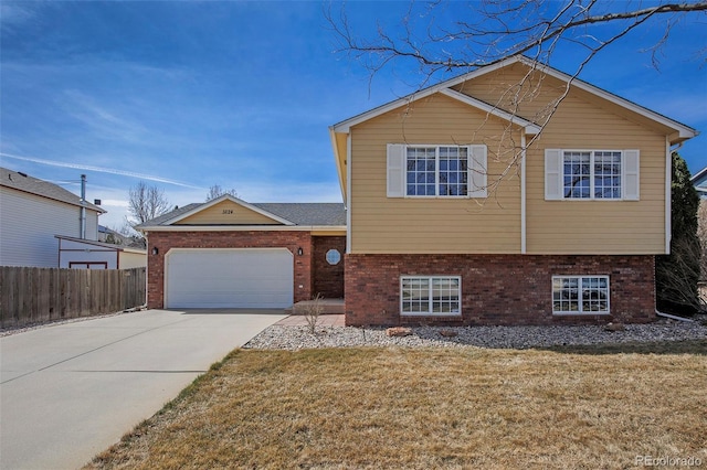 split level home featuring concrete driveway, fence, an attached garage, a front yard, and brick siding