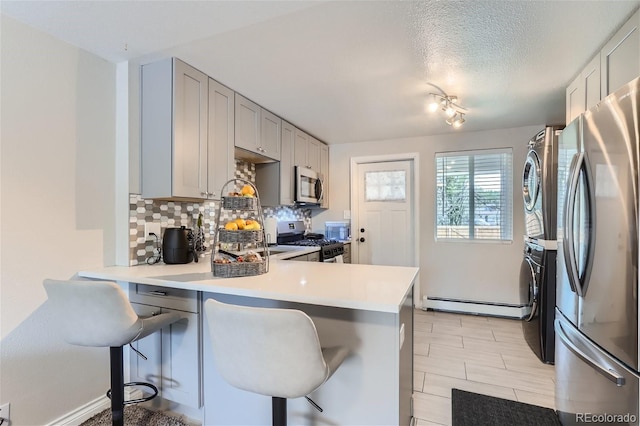 kitchen with stainless steel appliances, stacked washer and clothes dryer, a kitchen bar, and kitchen peninsula