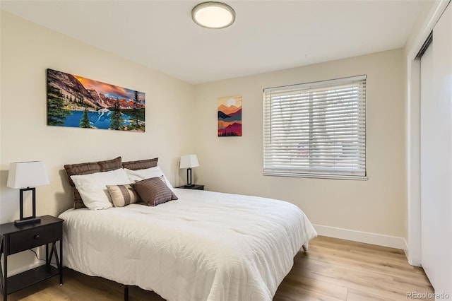 bedroom featuring baseboards, light wood-type flooring, and a closet