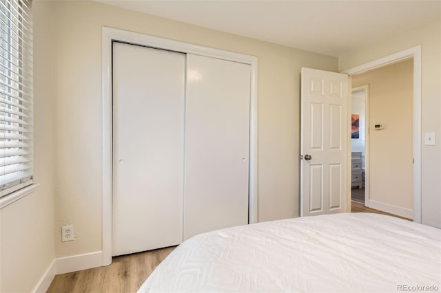 bedroom with a closet, light wood-style flooring, and baseboards