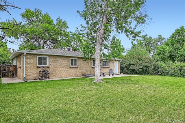 back of house featuring fence, brick siding, a lawn, and a patio area