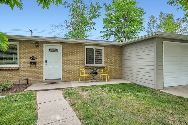 view of exterior entry with a garage, brick siding, and a yard