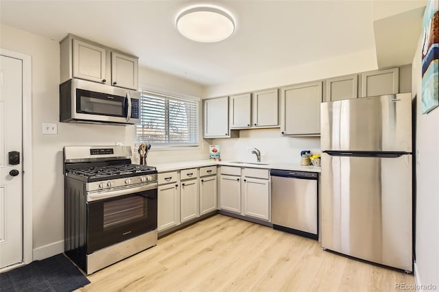 kitchen featuring light wood-type flooring, gray cabinets, a sink, stainless steel appliances, and light countertops