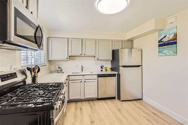 kitchen featuring baseboards, light wood-type flooring, light countertops, appliances with stainless steel finishes, and a sink