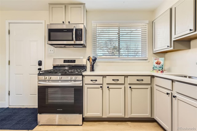 kitchen featuring appliances with stainless steel finishes, light wood-type flooring, light countertops, and a sink