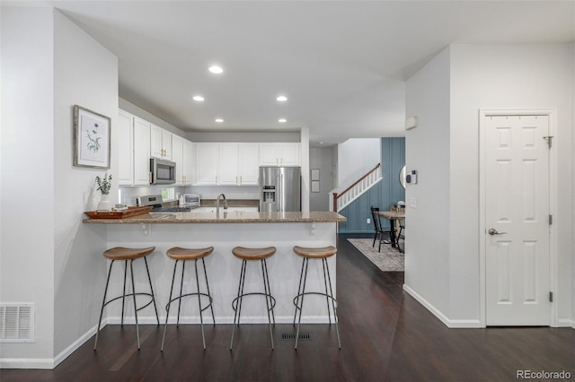 3433 N Wabash St, Denver, CO 80238 - kitchen with stainless steel appliances, a peninsula, dark wood-style floors, white cabinets, and a breakfast bar area